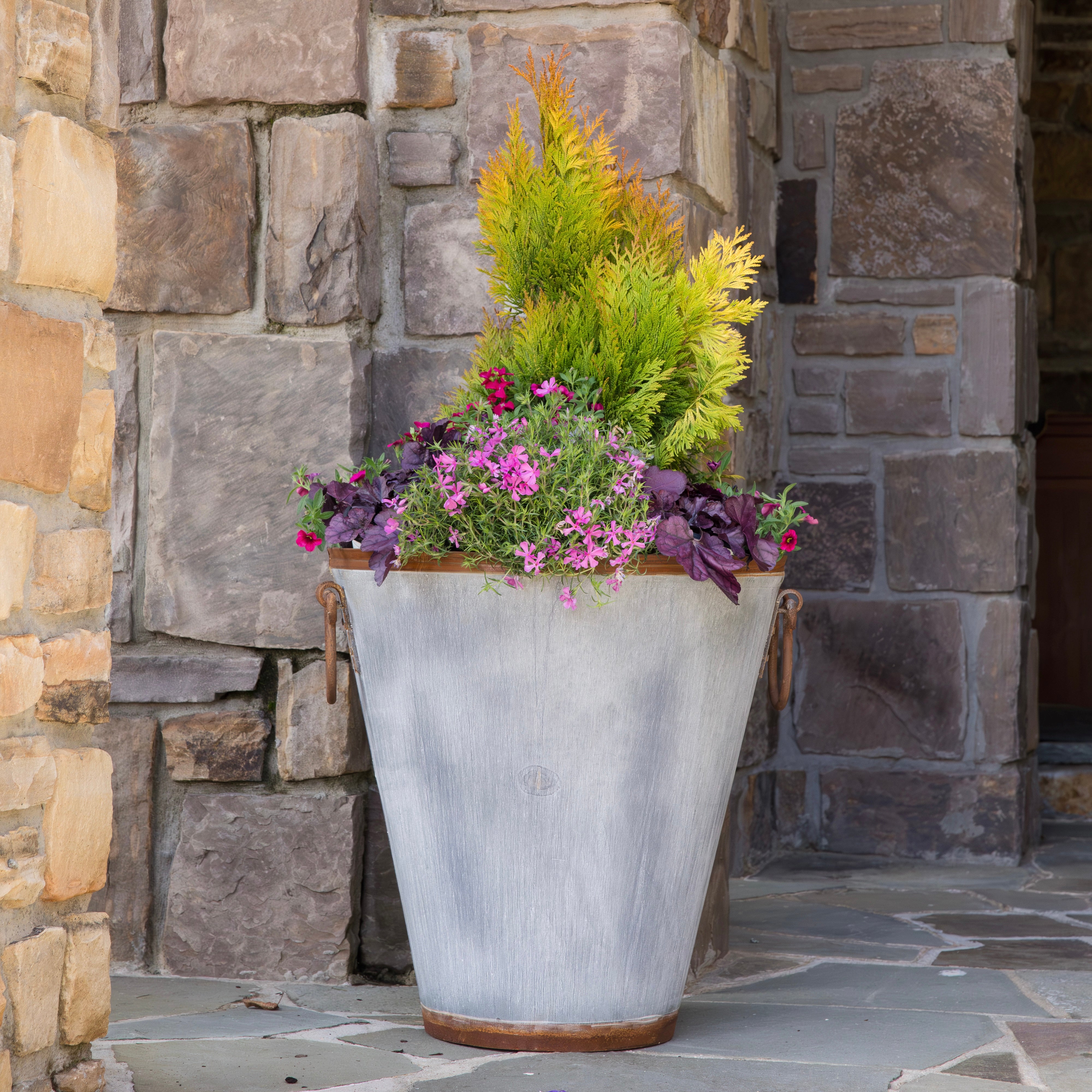 Decorative vintage inspired planter with greenery and flowers against a stone wall.