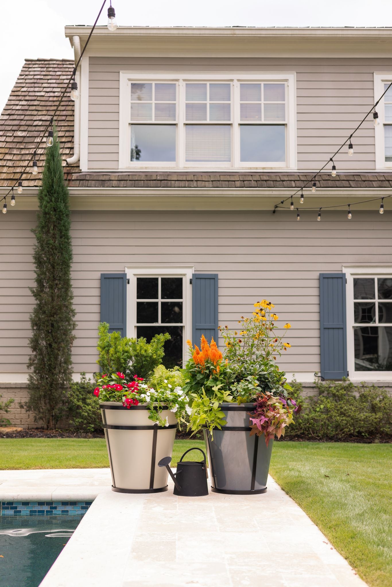 Potted plants on a patio in front of a house with a pool.