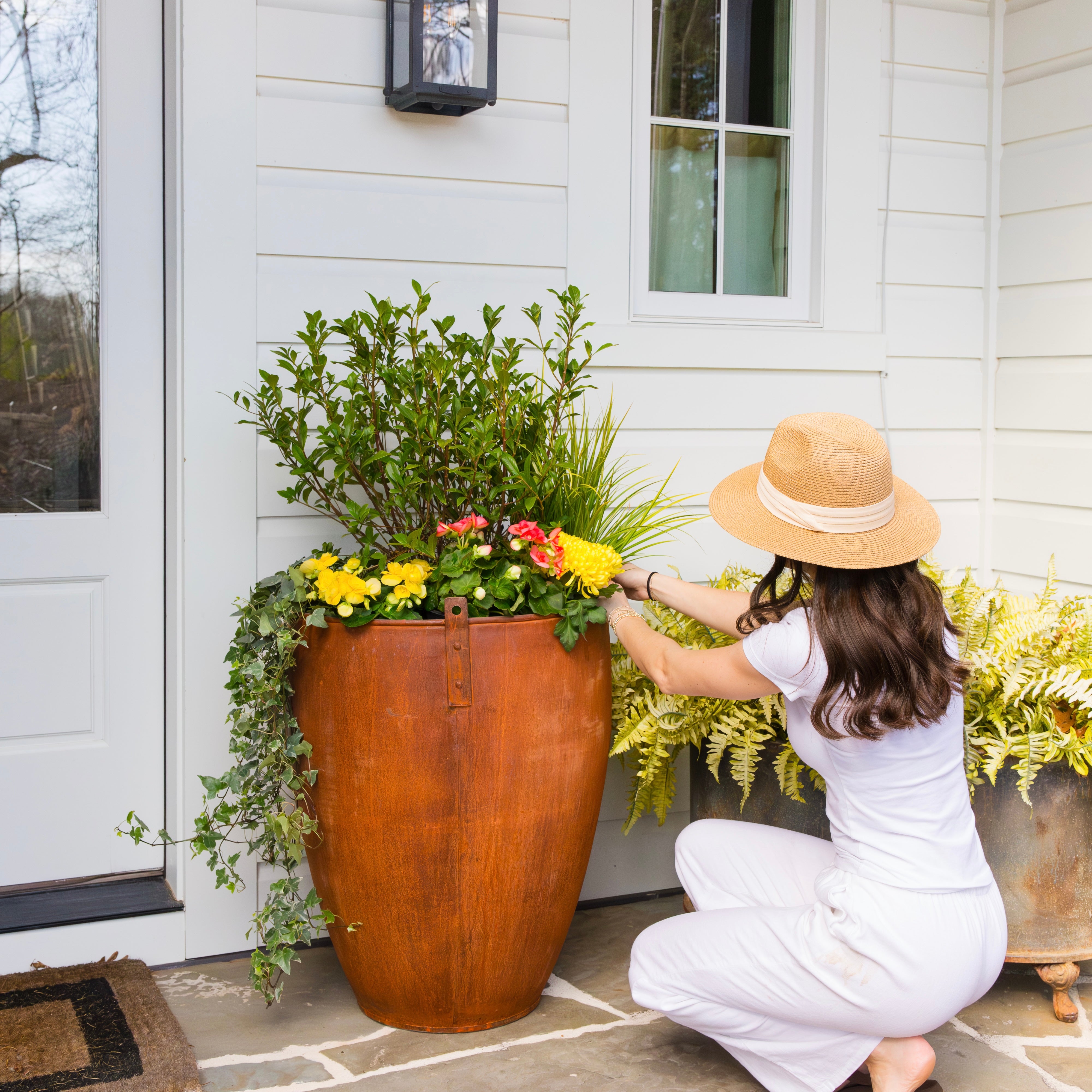 Person arranging flowers in a large decorative steel pot outside a house.