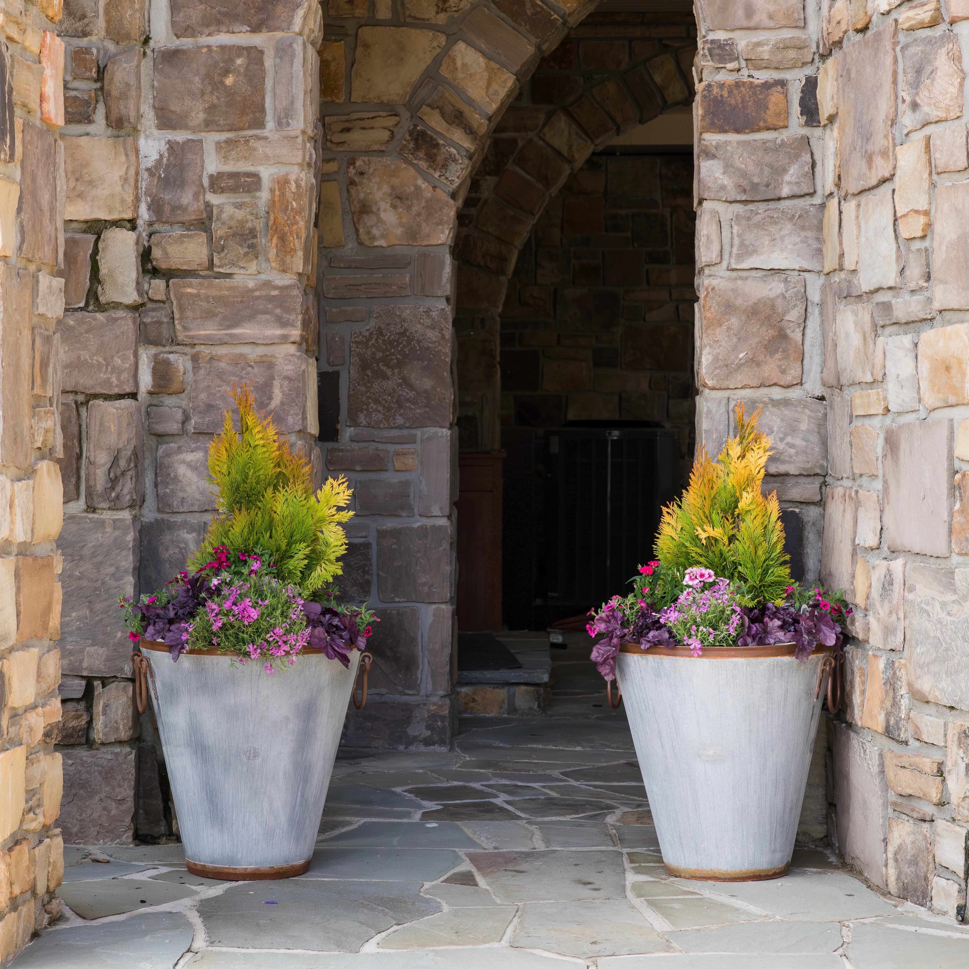 Two potted vintage honey bee outdoor planters in front of a stone archway