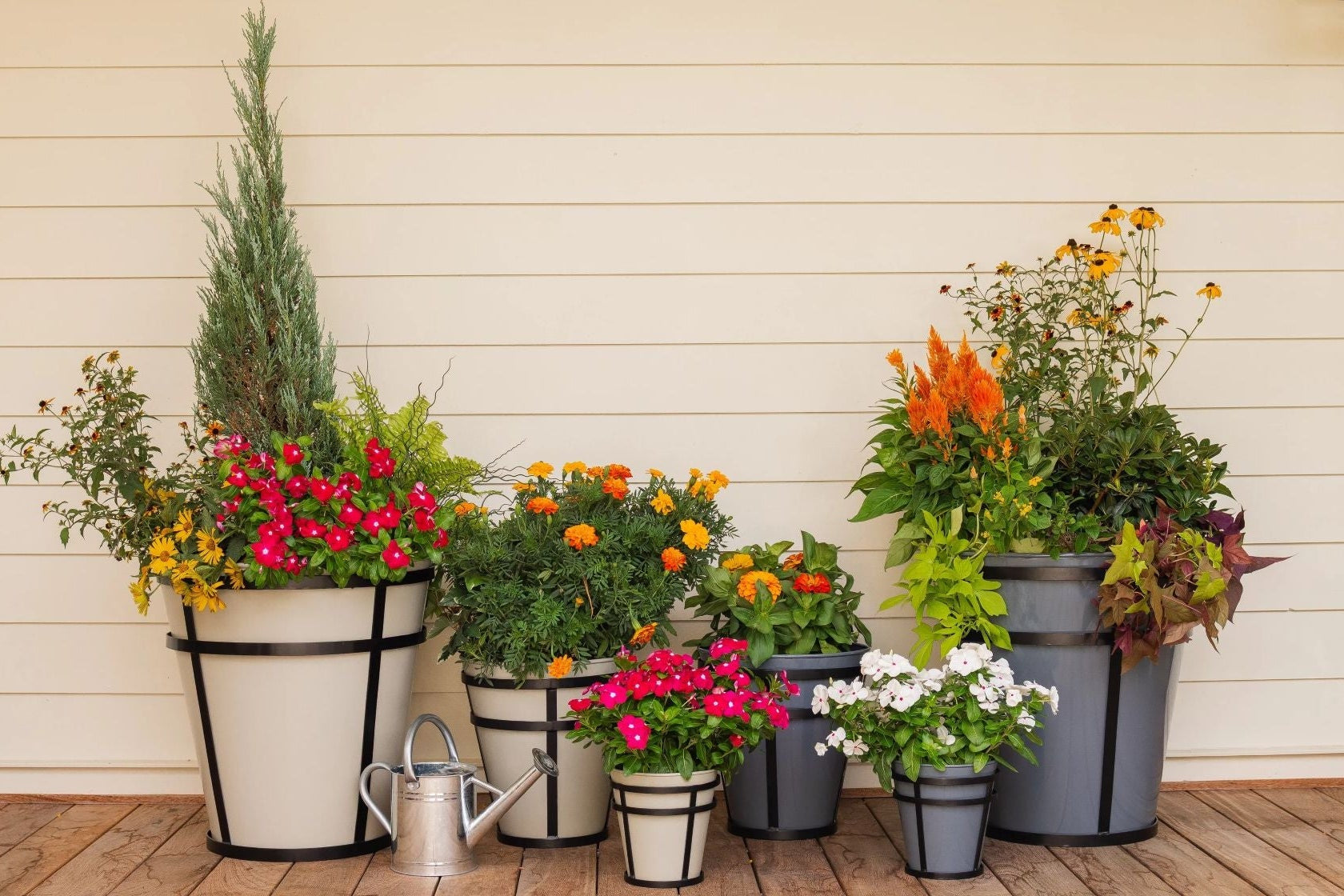 Collection of Honey Bee Outdoor potted metal planters on a wooden deck against a beige wall.