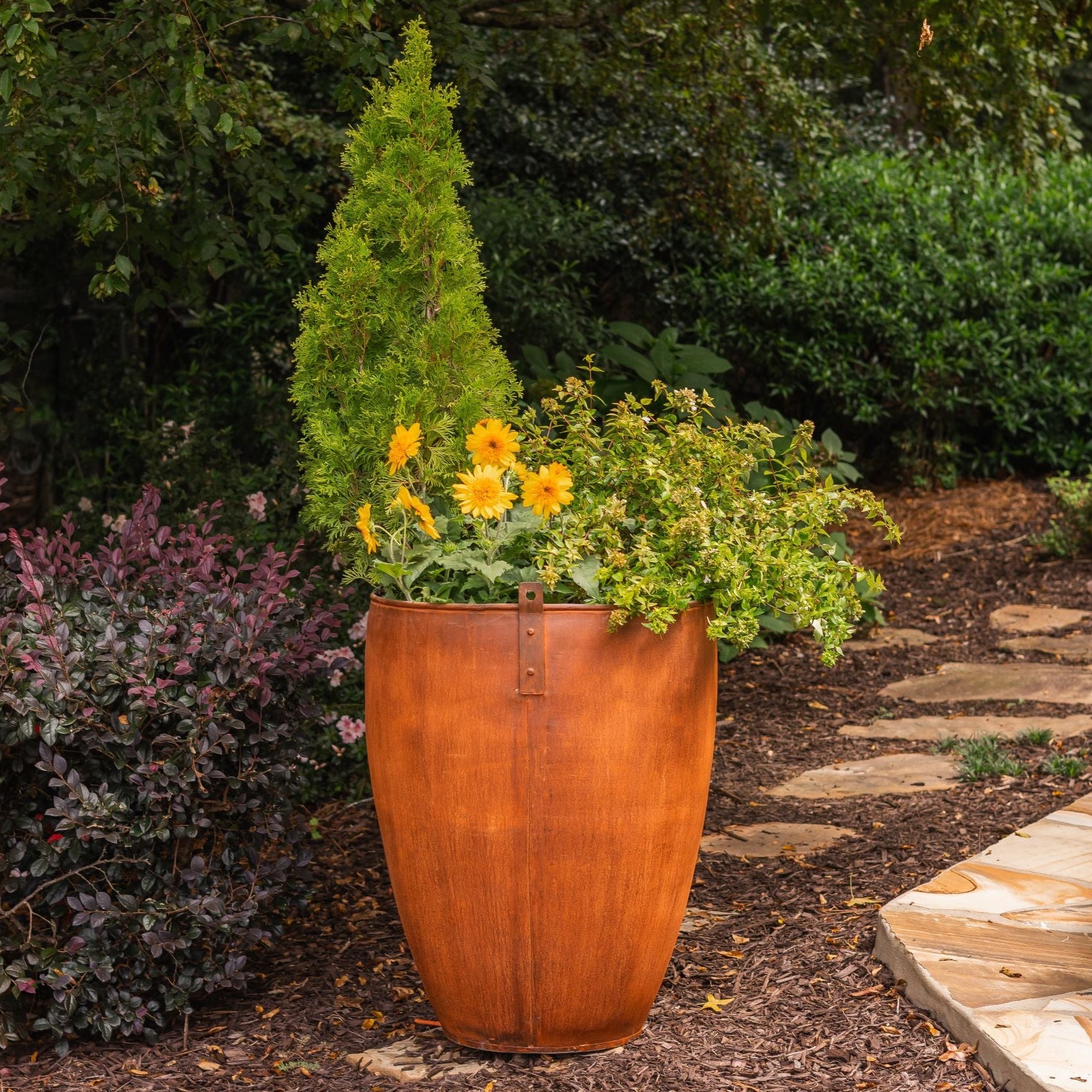 Decorative vintage planter with greenery and flowers in a garden setting.