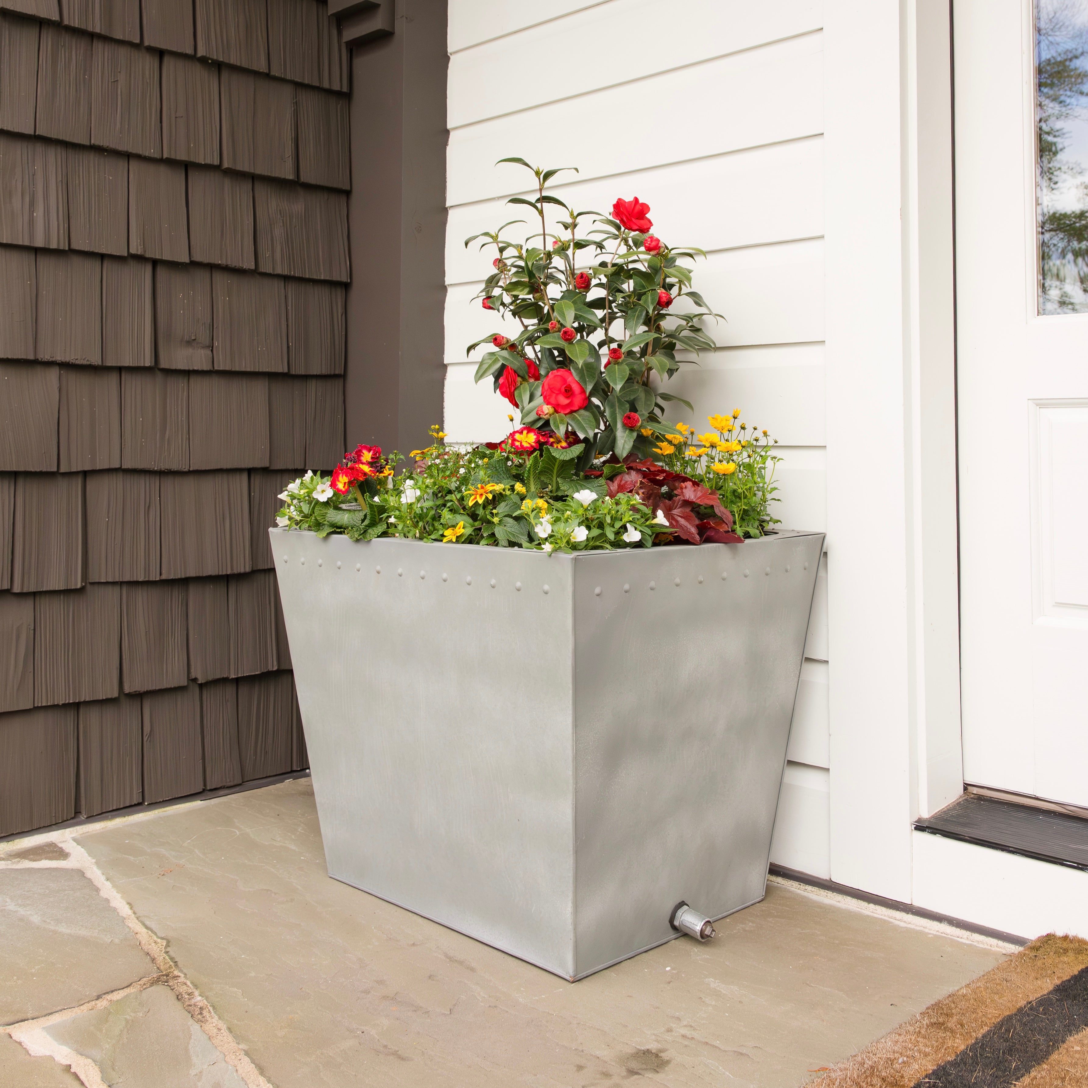 Decorative metal planter with flowers on a patio next to a house.