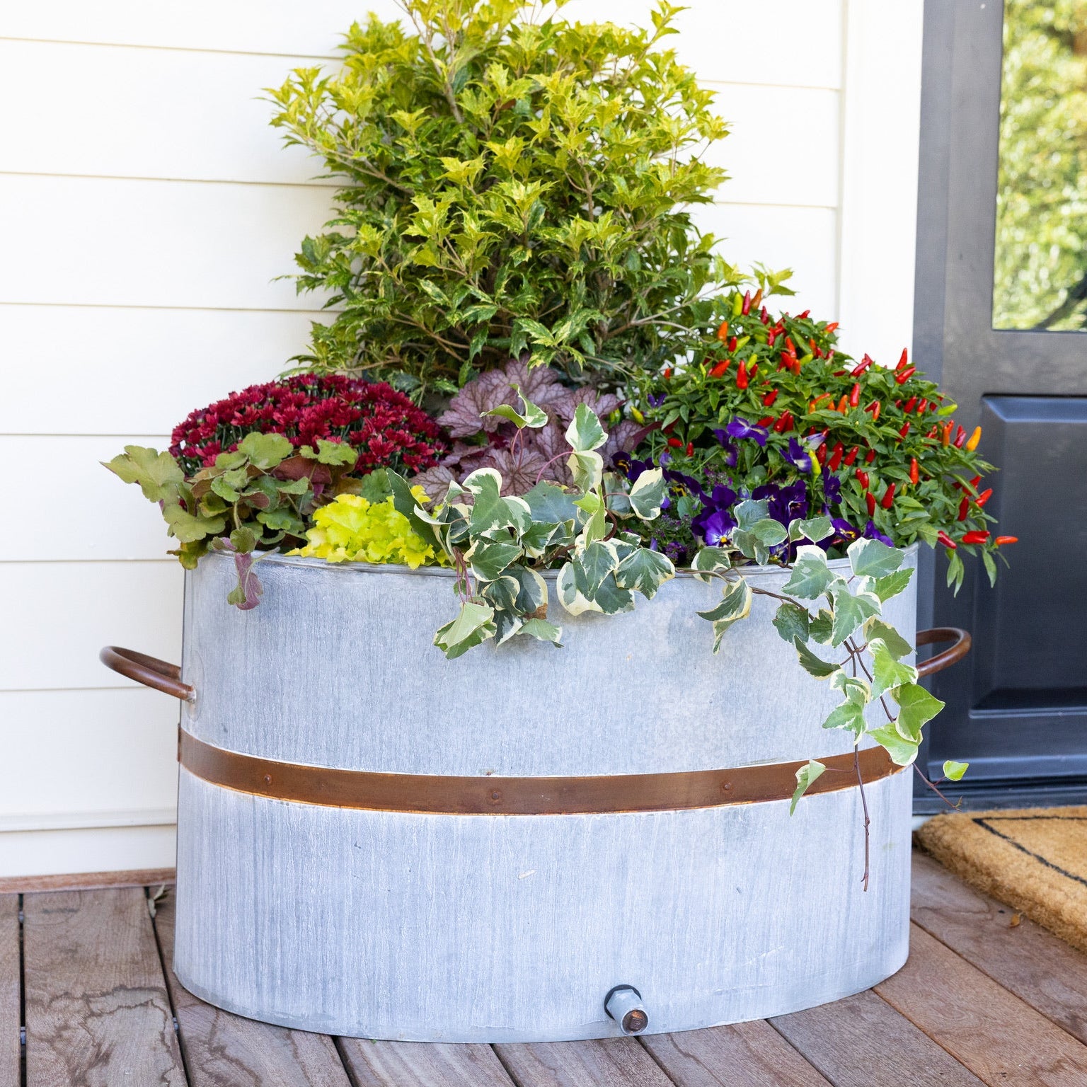 Decorative planter with flowers on a wooden deck in front of a house.