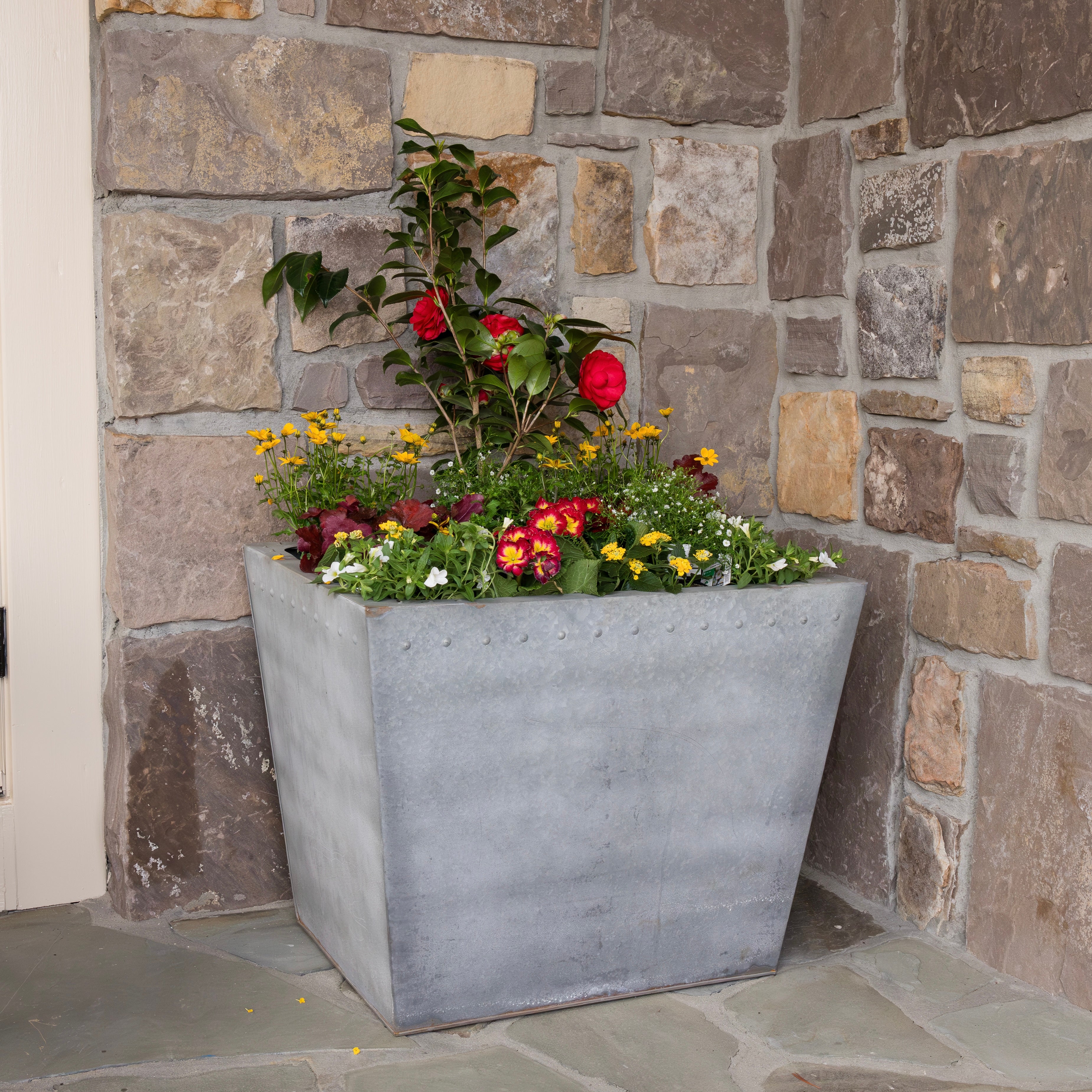 Floral arrangement in a steel planter against a stone wall.