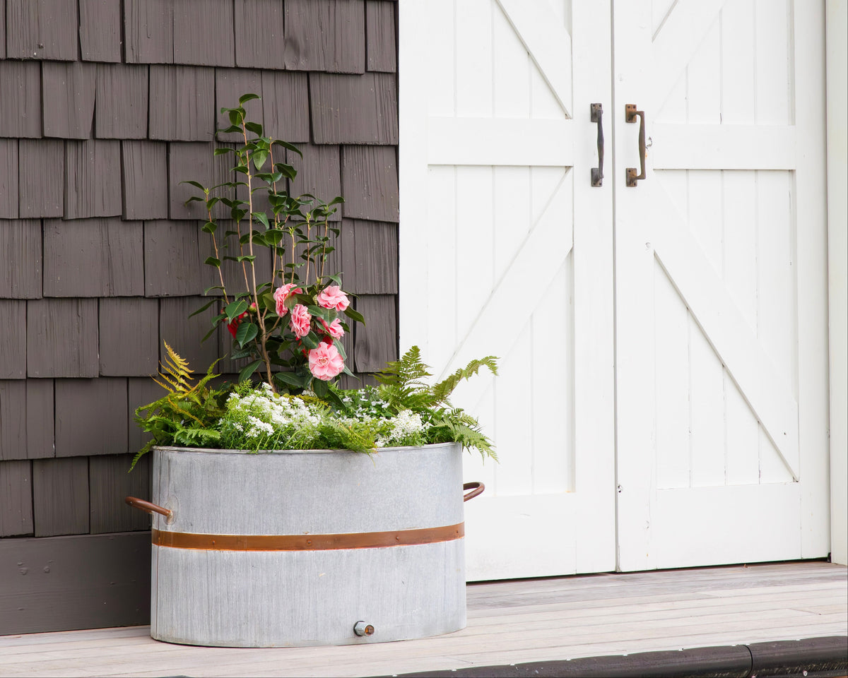 Decorative planter with flowers in front of a gray shingled wall and white doors.
