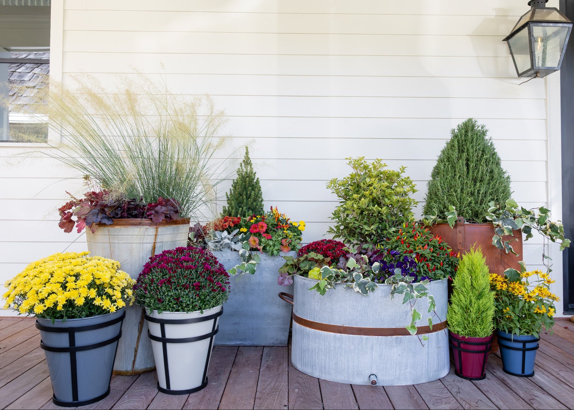 Decorative farmhouse porch with potted metal planters on a wooden deck.