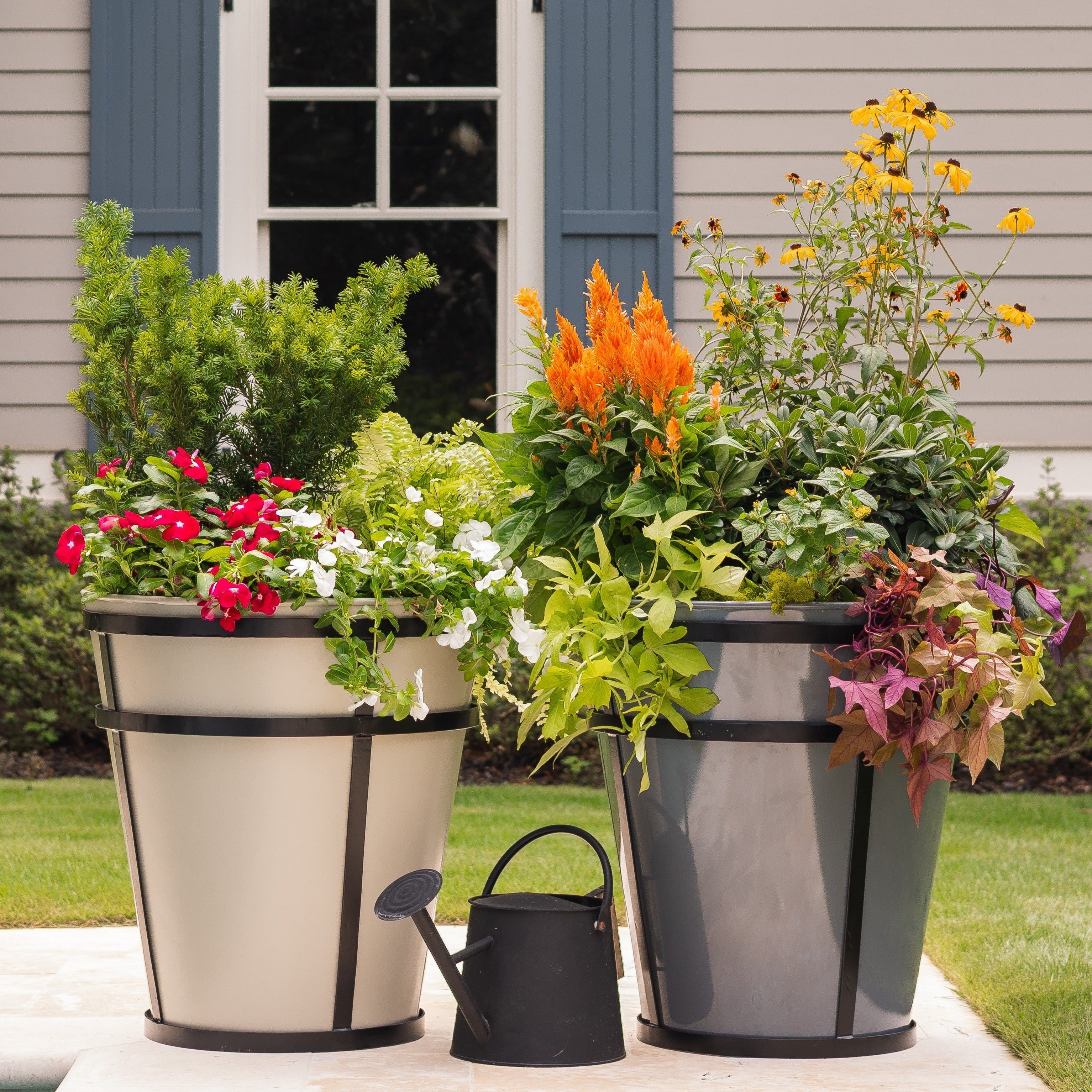 Two large steel planters potted with flowers next to a watering can.
