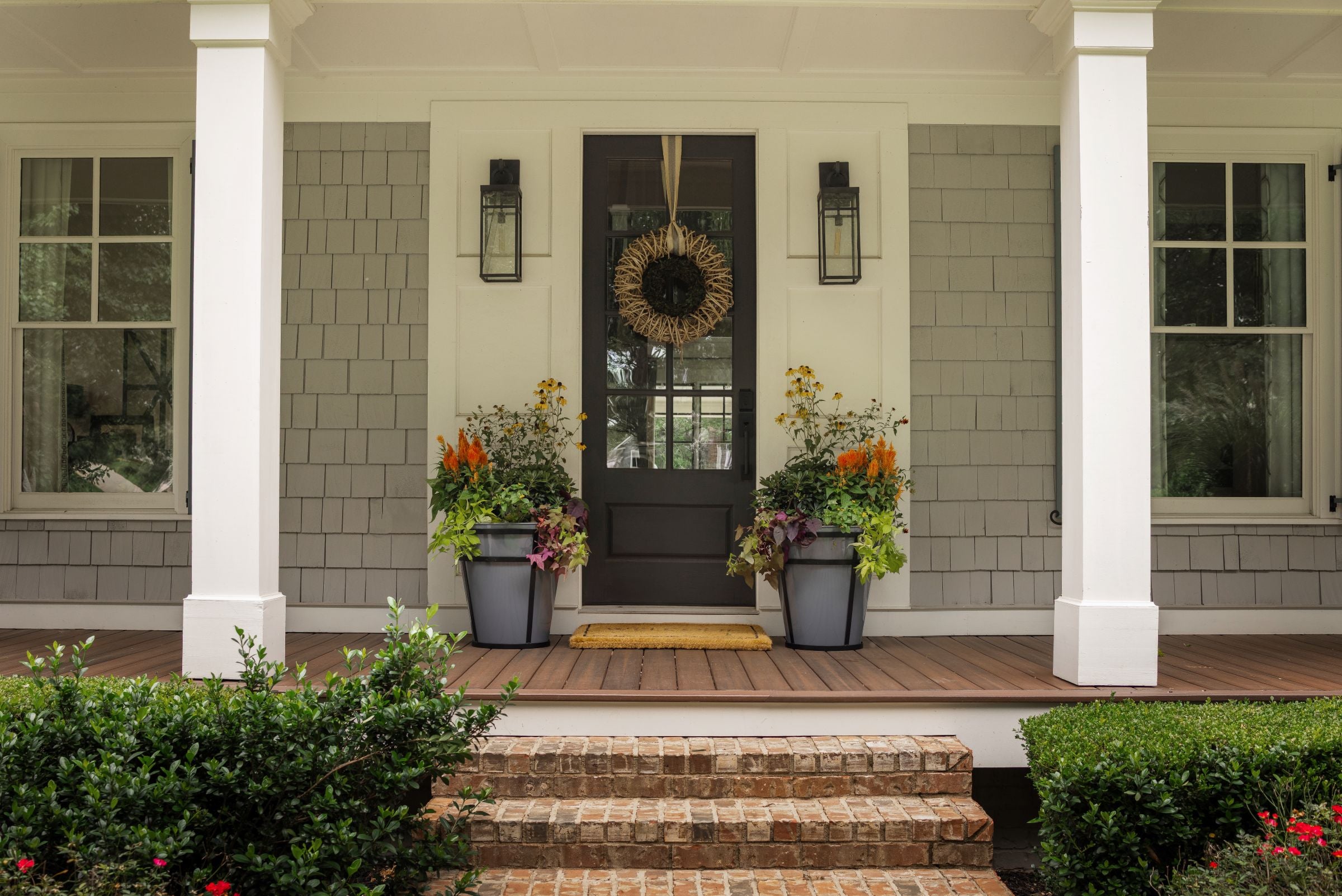 Front porch with decorative elements including a wreath, Honey Bee Outdoor potted planters, and a doormat.