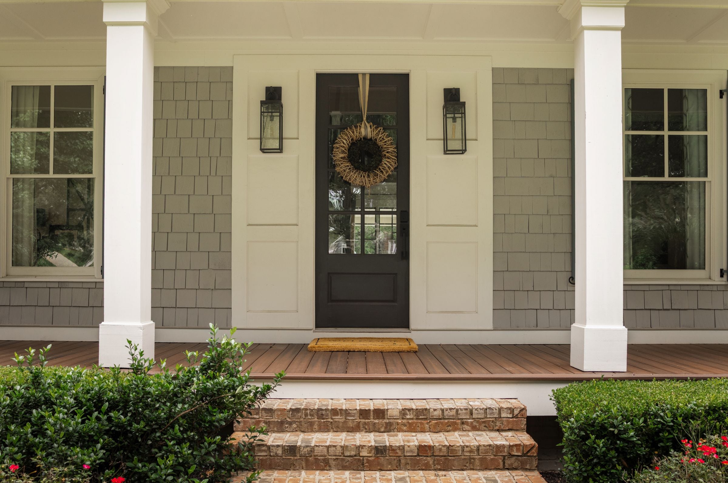 Front porch of a house with a wreath on the door, surrounded by greenery.