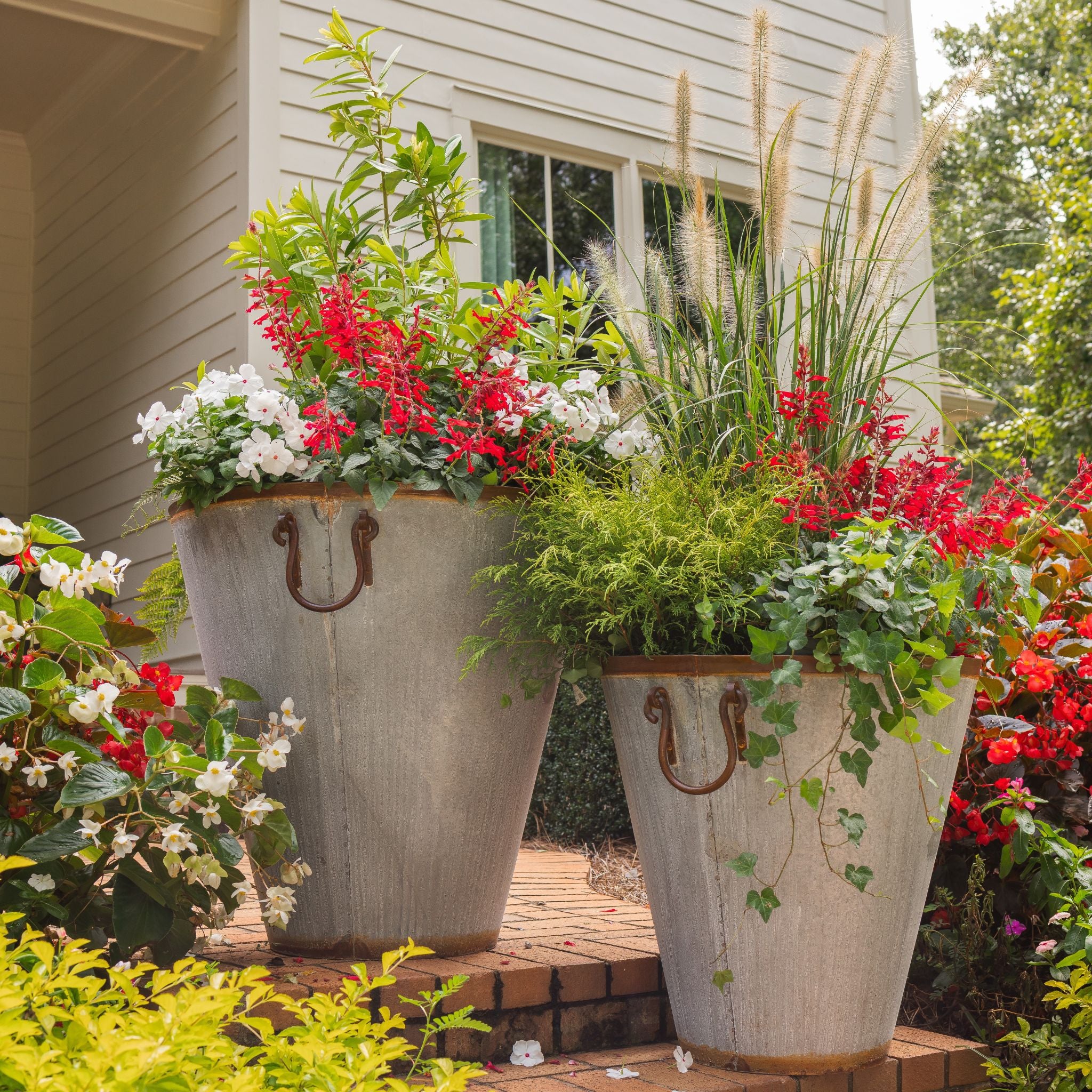 Large vintage outdoor metal planters with flowers and greenery in front of a farmhouse style house.