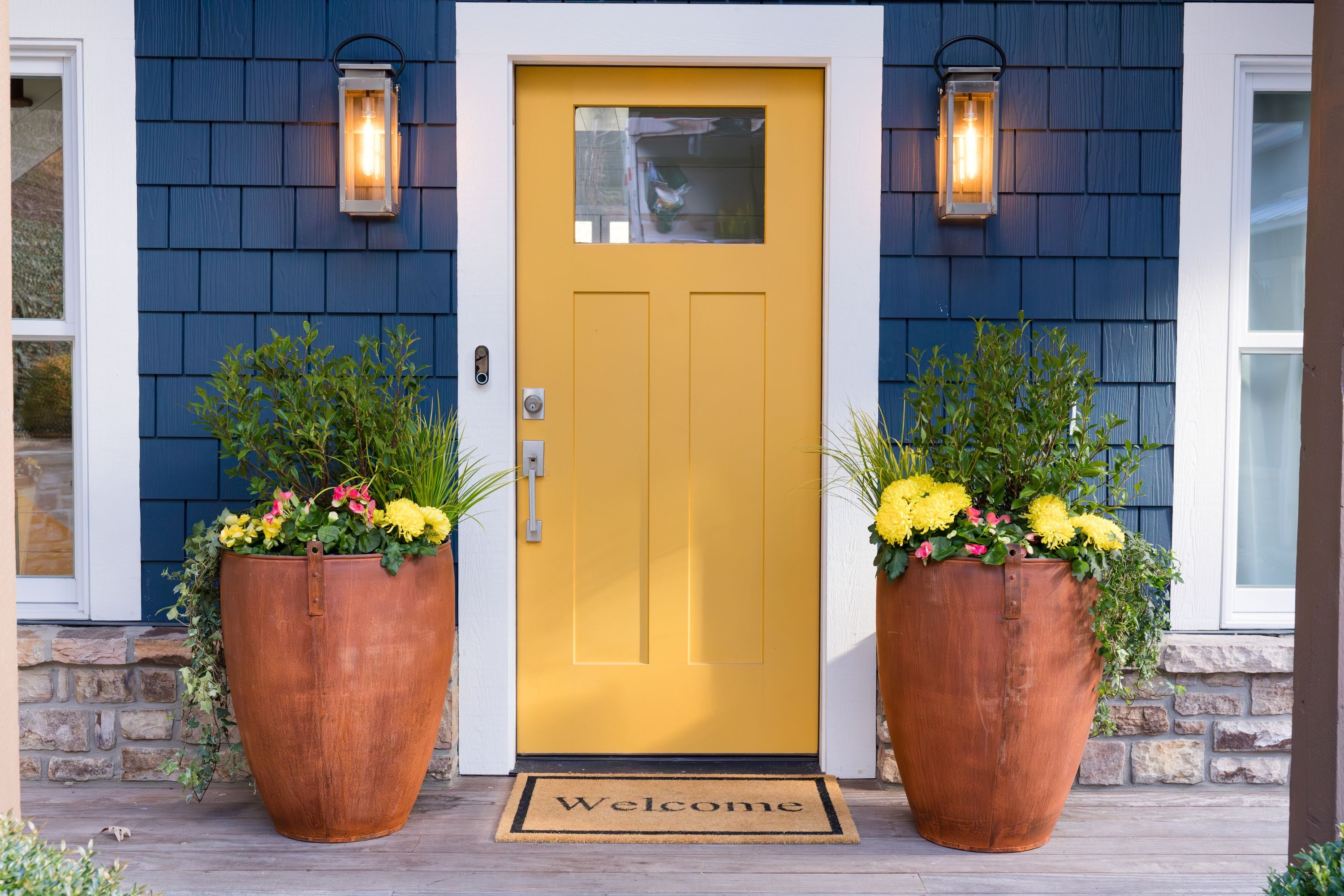 Yellow front door of a house with Honey Bee Outdoor unique decorative planters and a 'Welcome' mat.
