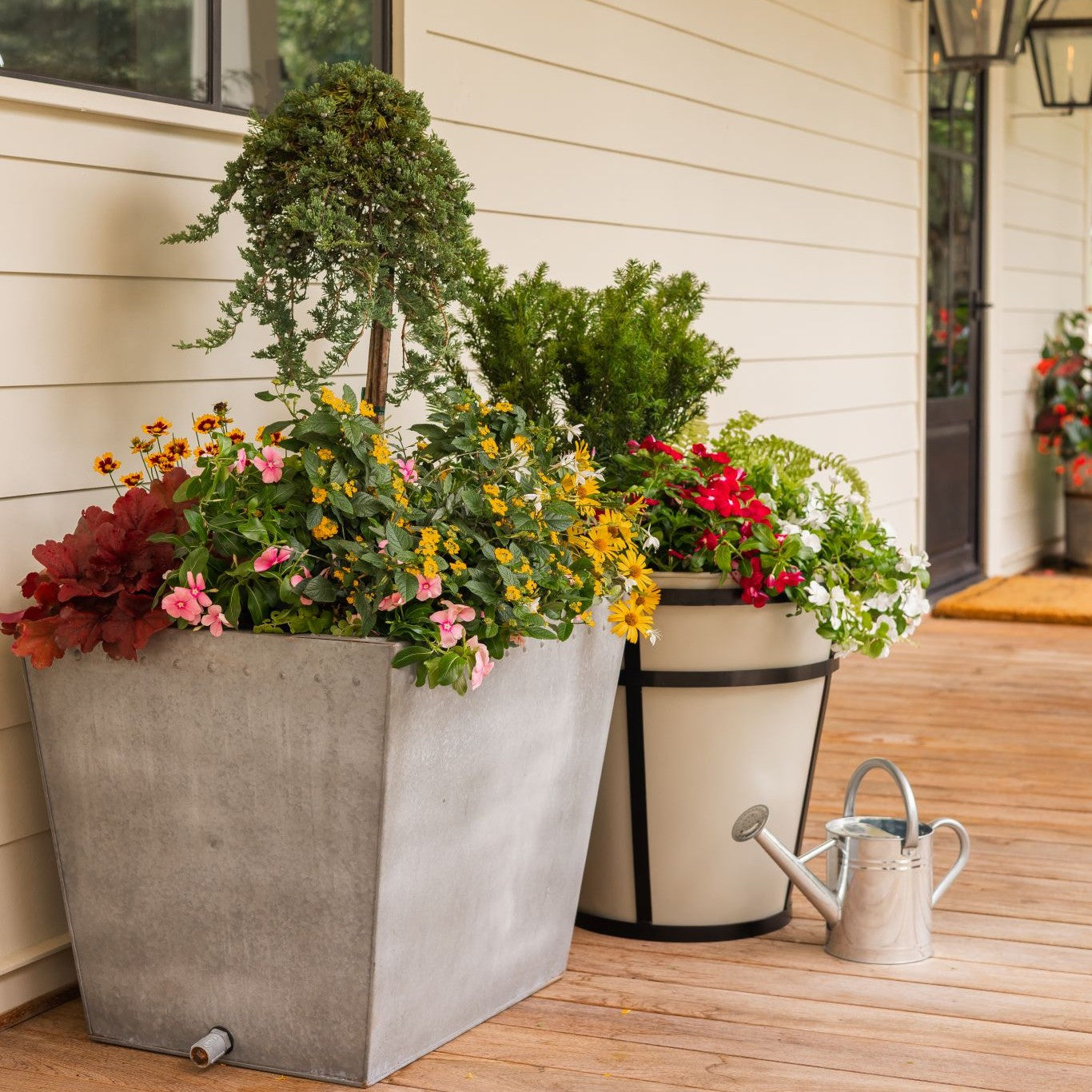 Decorative outdoor planters with flowers on a wooden deck next to a house.